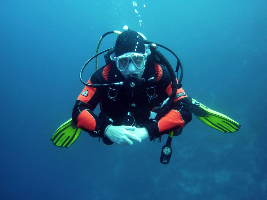 A scuba diver in a black and orange wetsuit, wearing a mask and snorkel, underwater with bubbles rising around them.