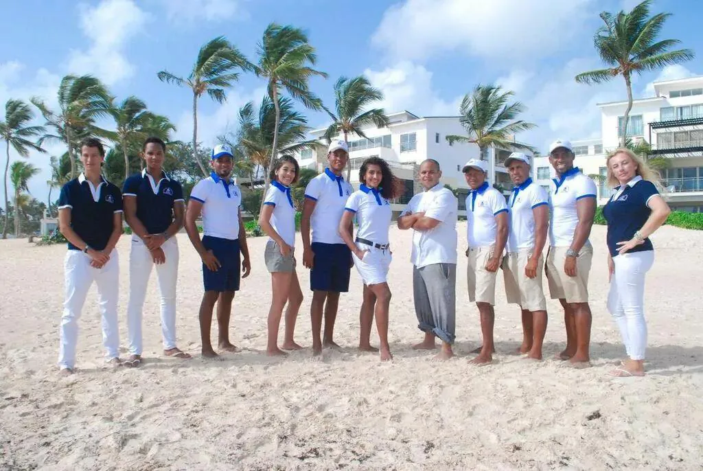 A team of eleven people in matching blue and white uniforms standing on a beach with palm trees and buildings in the background, representing the boat trip crew.